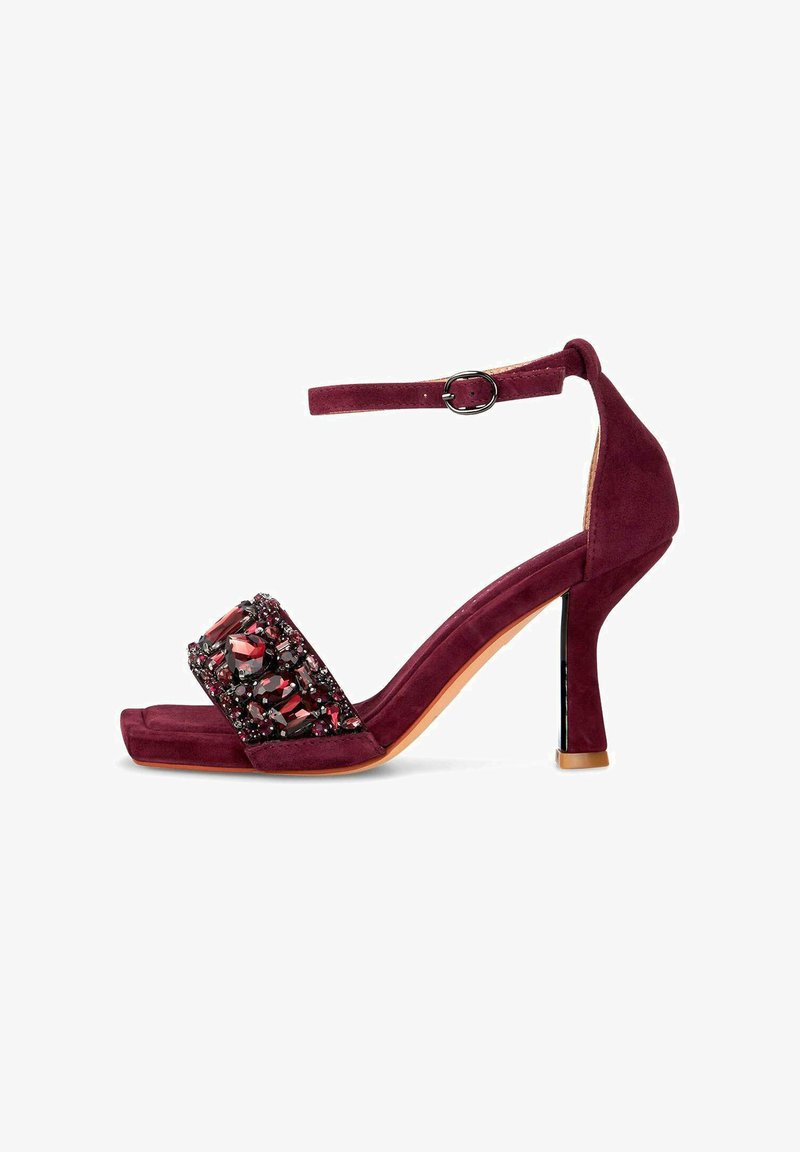 Burgundské velurové sandály na podpatku s dekorativním páskem zdobeným kamínky a sponou kolem kotníku. Podpatek je zúžený, což zvyšuje elegantní tvar.