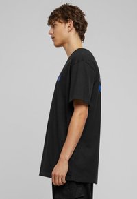 Sort bomulds-T-shirt med afslappet pasform, der har korte ærmer og rund halsudskæring. Et blåt hjertegrafik er trykt på brystet.
