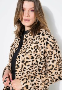 Jeanová bunda s leopardím potiskem, dvěma náprsními kapsami, černými knoflíky a uvolněným střihem, s světle hnědým pozadím a tmavými skvrnami.