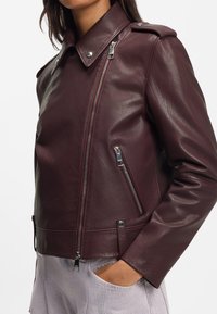 Burgundy leather jacket with a fitted shape, silver zippers, and snap button details on the collar and cuffs, featuring a smooth texture.