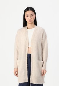 Cardigan lungo beige realizzato in un tessuto morbido e texture, con apertura frontale, polsini a coste e due tasche frontali.