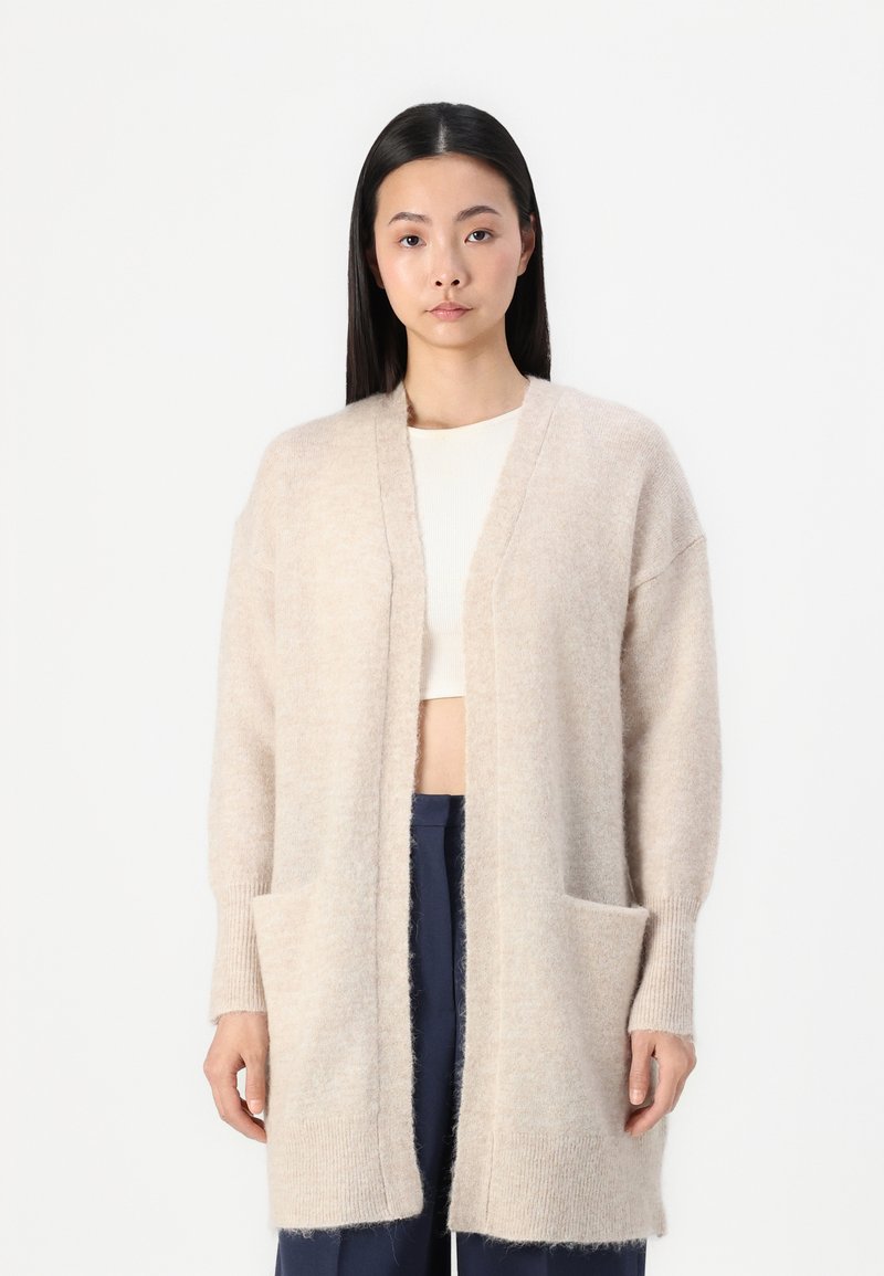 Cardigan lungo beige realizzato in un tessuto morbido e texture, con apertura frontale, polsini a coste e due tasche frontali.
