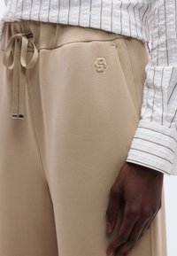 Beežid jogger-püksid pehme tekstuuriga, millel on reguleeritav nöörvöökoht ja ees peen reljeefne logo.