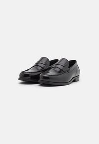 Mocasines de cuero negro con un acabado suave, costuras decorativas a lo largo de los bordes, una forma cómoda y un tacón bajo.