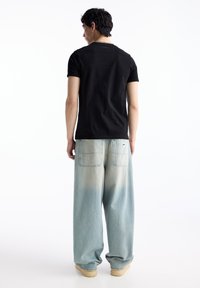 Tricou negru cu mânecă scurtă, asociat cu blugi din denim oversized de culoare bleu deschis, având decolorări, două buzunare la spate și pantofi bej.