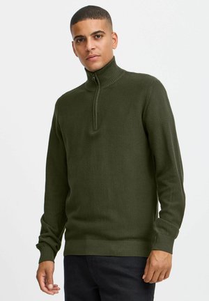 Olive green knit pullover with a high collar and zip, featuring textured fabric and ribbed cuffs and hem. Scaled pattern details visible.