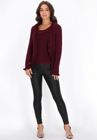 Bordowy kardigan w prążki z falbankami, noszony na pasującym topie, w zestawieniu z czarnymi legginsami i srebrnymi sandałami na obcasie z paskami.