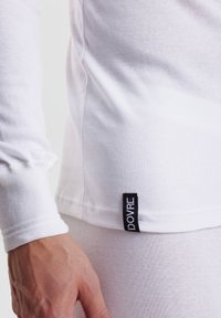 White long-sleeve shirt made of soft cotton, featuring a round neck, fitted sleeves, and a black label with "DOVRE" on the hem.