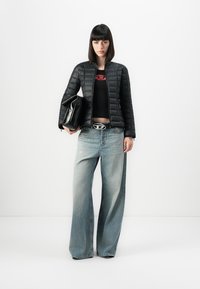 Svart quiltet jakke med rund hals, parret med en tettsittende svart crop top, løse lyseblå jeans, og holder en svart håndveske.