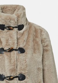 Beżowy płaszcz z sztucznego futra z wysokim kołnierzem, z czarnymi zapięciami toggles i skórzanymi akcentami, prezentujący miękką, teksturowaną powierzchnię.