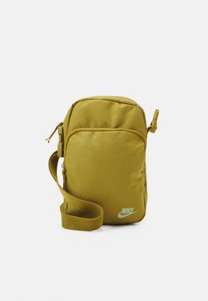Petit sac à épaule Nike jaune moutarde avec poche avant zippée et bandoulière réglable sur fond blanc.