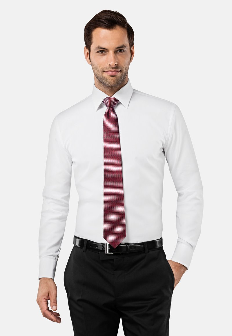 Witte dress shirt met een puntkraag, gecombineerd met een rode stropdas met een geruit patroon. Draagt zwarte broek en een zwarte riem.
