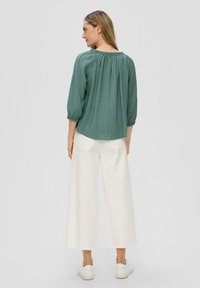 Groene textuur blouse met een geplooide halslijn en driekwartmouwen, gecombineerd met brede witte broeken en witte sneakers.