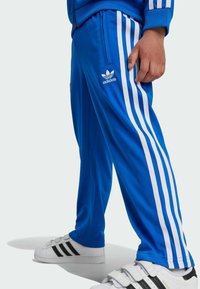 Blå, lätta polyester träningbyxor med vita sidostripes och en Adidas-logotyp. Har en rak benstil och fickor med dragkedja.