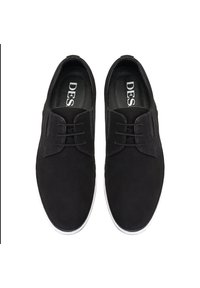 Chaussures en daim noires à finition lisse, avec un bout arrondi et une semelle en caoutchouc blanche, comportant des lacets et des détails de design minimalistes.