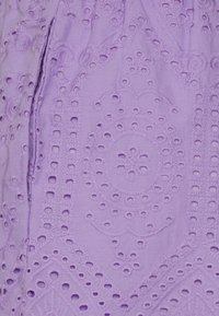 Tissu lavande avec un motif brodé détaillé de fleurs et d'œillets circulaires.