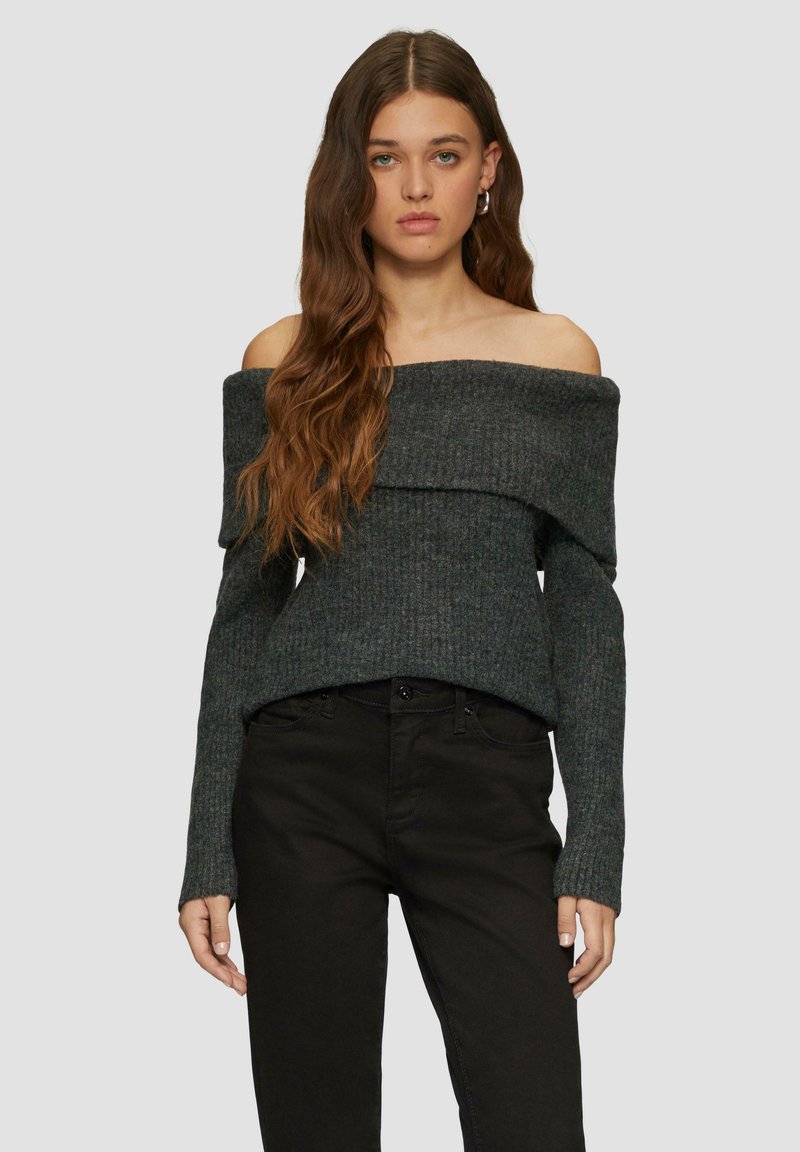 Dunkelgrauer, gerippter Pullover mit schulterfreiem Schnitt, umgeschlagenem Kragen und langen Ärmeln, kombiniert mit eng anliegenden schwarzen Jeans.