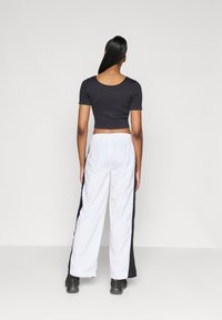 �Černý zkrácený top s krátkým rukávem a kulatým výstřihem, zkombinovaný s bílými širokými kalhotami s černými bočními pruhy a měkkou texturou.