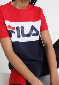 Tričko s barevnými bloky v červené, bílé a námořnické barvě vyrobené z bavlny, s velkým logem FILA na prsou. Krátké rukávy a kulatý výstřih.