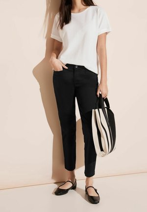 Weißes, strukturiertes Kurzarmoberteil, schwarze enganliegende Hose, schwarze flache Schuhe und eine schwarz-weiß gestreifte Tragetasche. Einfaches und modernes Outfit.