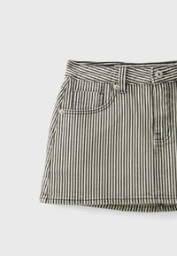 Mini-jupe en denim rayée verticalement noir et blanc avec poches avant, passants pour ceinture et fermeture par bouton sur fond blanc.