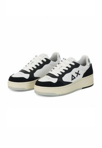 Sneaker basse bianche e nere realizzate in materiali scamosciati e in pelle, dotate di un logo triangolare, chiusura con lacci e suola in gomma.