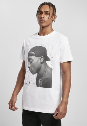 T-shirt en coton blanc présentant un grand graphique portrait noir et blanc d'une figure portant une casquette, avec un fond texturé et un détail de chaîne.