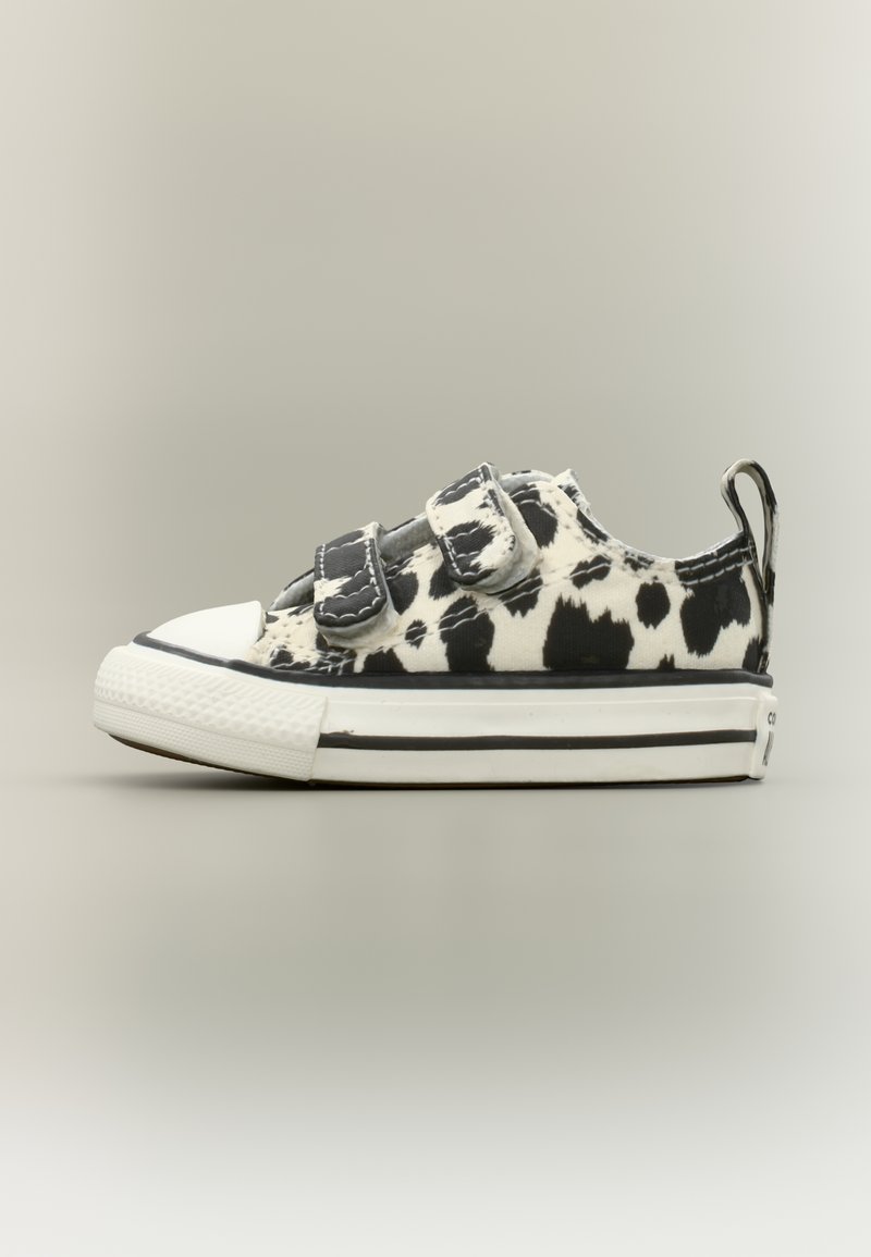 Χαμηλού τύπου αθλητικό παπούτσι με ύφασμα σε εκτύπωση με μοτίβο μαύρου και άσπρου αγελάδας, δύο λουράκια με βέλκρο, λαστιχένιο άσπρο κάλυμμα δακτύλων και παχύ λευκό πέλμα με μαύρες ρίγες.