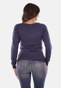 Maglione lavorato a maglia di colore blu navy con maniche lunghe e collo a V. Il tessuto appare liscio, aderente in vita e presenta polsini e orlo a costine.