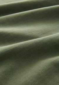 Cotton fabric in muted olive green, featuring a smooth texture with slight ribs and gentle folds creating a subtle play of light.