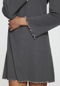 Abito grigio in maglia a maniche lunghe con bordo bianco arruffato sui polsini e sull'orlo. Il tessuto sembra morbido e leggero.