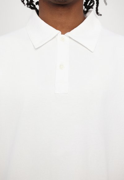 White polo shirt with a pointed collar, featuring two buttons and a smooth cotton texture. Clean and simple design, no patterns or accents.