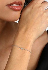 Silverfärgad kedjeband med ett delikat hjärtanhänge, med en tvinnad design och en slät, glänsande yta.