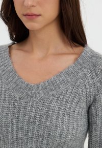 Szary sweter z dzianiny o ryflowanej fakturze i szerokim dekolcie w kształcie litery V, wykonany z miękkich włókien i w luźnym kroju.
