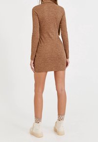 Robe longue marron à manches longues, côtelée, avec un col montant, une coupe cintrée et une longueur mi-cuisse, associée à des bottes crème et des chaussettes à motifs.