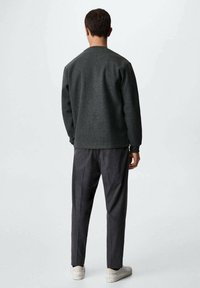 Grauer Pullover mit Rundhalsausschnitt aus strukturiertem Material; kombiniert mit dunkelgrauen, maßgeschneiderten Hosen und weißen Sneakers.