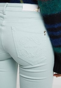 Licht mintgroene jeans met een gestructureerde, slim fit. Kenmerkt zich door een geborduurde achterzak met "PATRIZIA PEPE" en twee zilveren accenten.