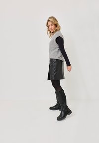 Gray wool sleeveless sweater over a black long-sleeve top, paired with a black leather skirt and knee-high black boots with buckles.