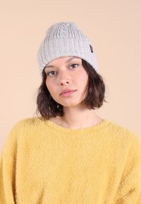 Bonnet en tricot beige avec un motif de câble texturé, doté d'un bord côtelé et d'une petite étiquette logo. Matériau chaud et doux.