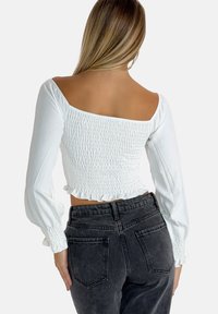 Top blanc court avec texture smockée, manches longues bouffantes et décolleté carrée. Assorti à un jean foncé taille haute.