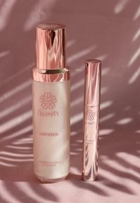 Due fiale di siero su uno sfondo rosa chiaro. La fiala più grande è di un colore crema con un tappo cromato e rosa, etichettata "Siero per Capelli". La fiala più piccola, anch'essa cromata e rosa, è etichettata "Siero per Ciglia e Sopracciglia".