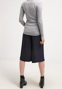 Haut gris à manches longues associé à un pantalon culotte bleu marine, mettant en valeur une texture lisse. La tenue est complétée par des bottines noires.