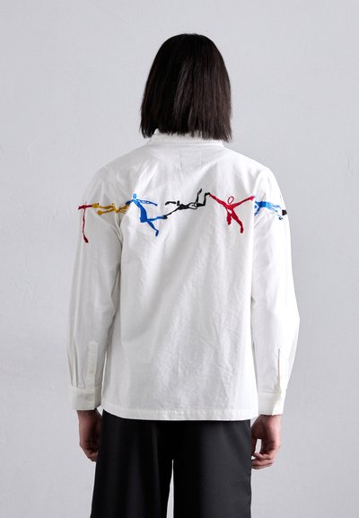 White shirt featuring colorful embroidered figures in blue, red, yellow, and black across the upper back. Long sleeves with button details.