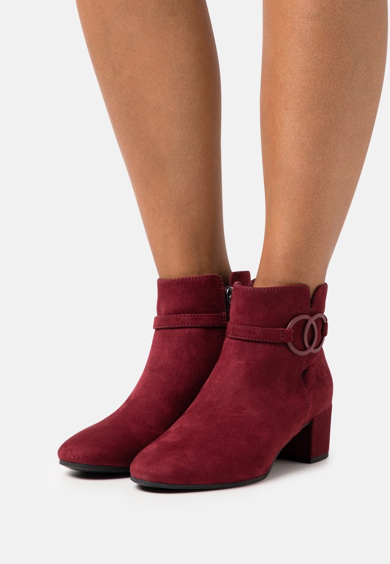 Bottines en suède bordeaux avec un bout arrondi, un col festonné, une fermeture éclair sur le côté et un accent décoratif en double cercle sur la sangle. Talon bloc.