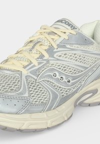 Ανοιχτό γκρι και κρεμ αθλητικό παπούτσι Saucony με πλέγμα, συνθετικά επικάλυψη, μπεζ κορδόνια και υφή σόλας, φτιαγμένο για τρέξιμο, από πλευρική όψη.