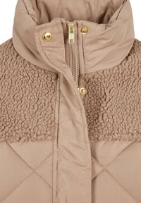 Beige Daunenjacke mit einem strukturierten, plüschigen oberen Abschnitt. Sie verfügt über einen hohen Kragen, goldene Reißverschlüsse und ein diamantgeplüstertes Muster im unteren Teil.