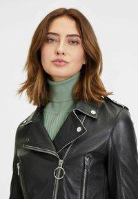 Schwarze Lederbikerjacke mit silbernen Reißverschlüssen und Druckknöpfen, die über ein zweireihiges Design, kontrastierende weiße Nähte und einen runden Reißverschlusszug verfügt.