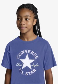 Μπλε βαμβακερό T-shirt με μεγάλο λευκό αστέρι και το κείμενο «CONVERSE ALL STAR» σε καμπύλη, αντιθετικά χρώματα. Απλό σχέδιο με κοντά μανίκια.