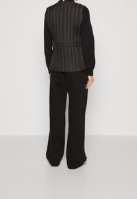 Gilet trapuntato nero con un design aderente e colletto alto. Abbinato a pantaloni neri a gamba larga, entrambi con una texture liscia.