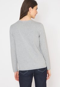 Maglietta grigia a maniche lunghe realizzata in tessuto morbido, con scollatura rotonda e vestibilità ampia. Abbinata a pantaloni in denim scuri.
